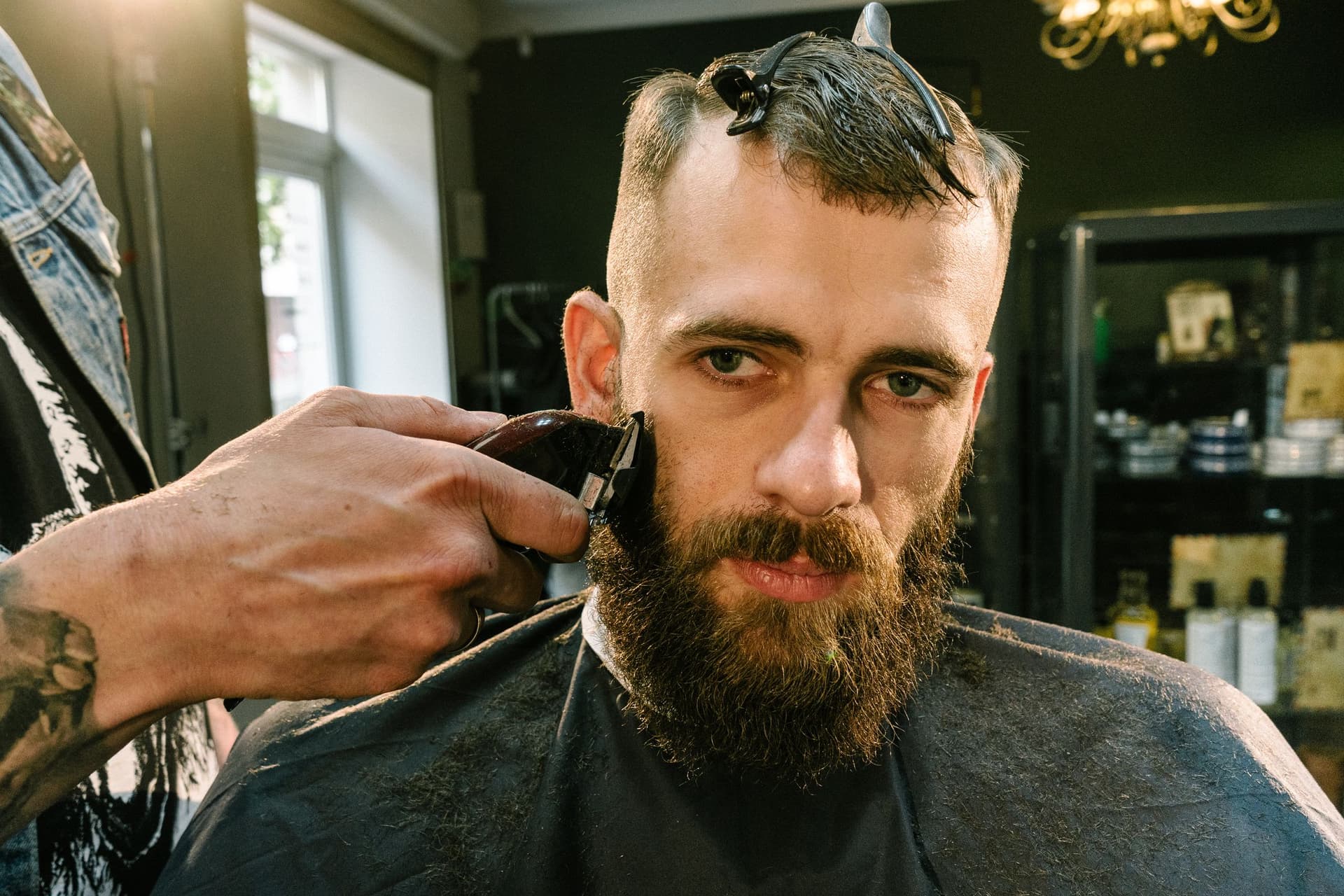A barber trimming a client's beard with clippers